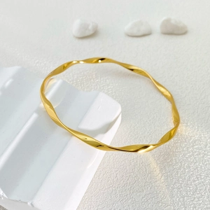 Detail of a gold Mobius bangle with a polished twisted design on a white platform