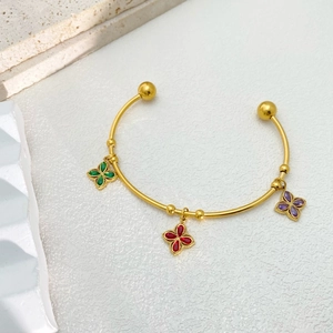 Detail of golden open bangle with green red and purple flower charms on stone surface