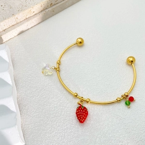 Detail of golden open bangle with strawberry and star charms on stone surface