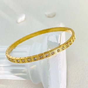 Dettaglio bracciale geometrico dorato con zirconi incastonati su una colonna bianca