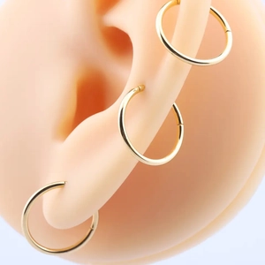 Macro view of three gold seamless 316L stainless steel hoops on a silicone ear model