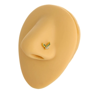 Detailed view of L-shaped gold butterfly nose stud with green and white zircons