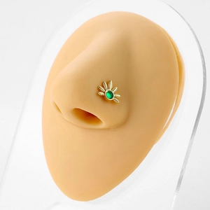 Gold 20G L-shaped nose stud with sunburst design and green emerald-style gem