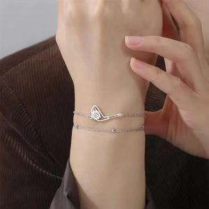 Detail eines silbernen doppellagigen Armbands mit Golfschläger- und Ballanhänger