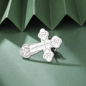 Close-up of orthodox stainless steel cross brooch with white enamel and religious engravings