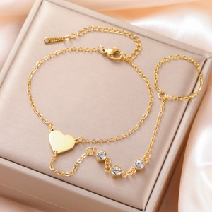 Detailed macro view of gold heart charm hand chain with sparkling crystals on champagne silk