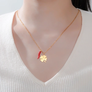 Detalle del collar de acero dorado con colgantes de chile rojo cornicello y trébol