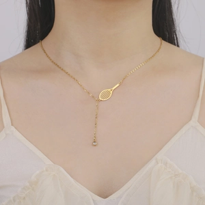 Primo piano di una collana a racchetta da tennis dorata con gemma indossata da modella