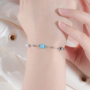 Detail view of dainty silver beaded bracelet with turquoise and pearl charms on wrist