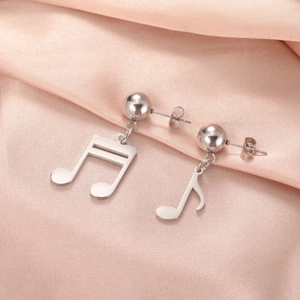 Primer plano de pendientes de nota musical de plata sobre elegante tela de seda rosa