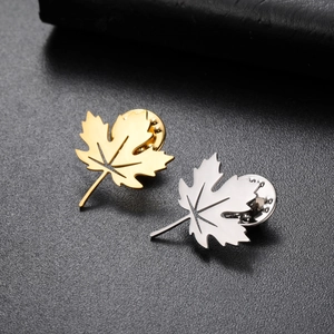 Macro detail of gold and silver maple leaf brooches with butterfly clutches on leather