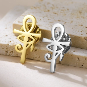 Macro shot of gold and silver Ankh and Eye of Horus lapel pins on beige stone
