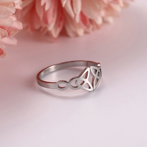 Detailed close-up of a silver Celtic Triquetra knot ring on a soft pink floral background