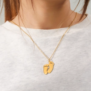 Detail einer goldenen Fußabdruck-Halskette, die ein Model auf einem weißen T-Shirt trägt