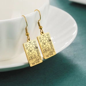 Detail of The Star Tarot card earrings in gold finish hanging on a white ceramic cup