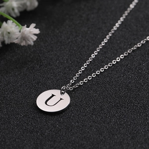 Detailed close-up of a silver round pendant with engraved letter U on a fine cross chain