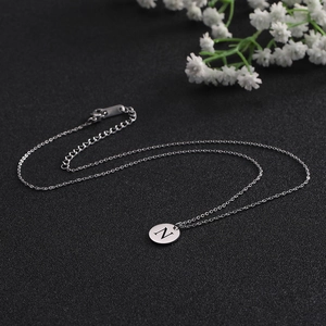 Detail of silver round pendant necklace with engraved letter N on black textured background