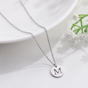 Macro view of silver round pendant with engraved M letter on minimalist chain