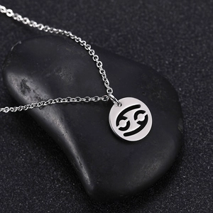 Macro shot of silver Cancer zodiac pendant necklace on black stone display background