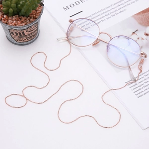 Détail de la chaîne de lunettes en métal perlé or rose sur fond de magazine blanc