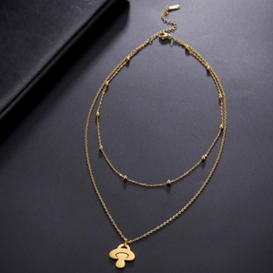 Détail d'un collier doré à double chaîne avec un pendentif champignon poli sur fond noir mat