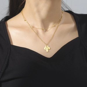 Gros plan d'un collier double épaisseur doré avec pendentif champignon minimaliste au cou