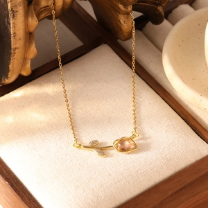 Detail van een gouden tulp hanger ketting met roze kattenoogsteen en zirkoon op houten blad