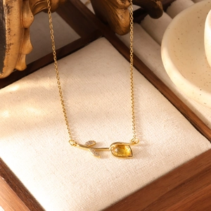Detail van gouden tulphanger met gele edelsteen en zirkoon op een fijne ketting