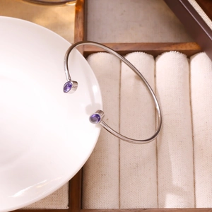 Dettaglio del bracciale argento aperto con gemme viola su ceramica bianca