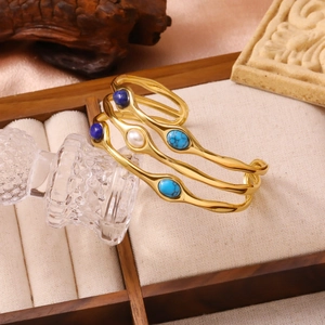 Nahaufnahme goldene Edelstahl-Armreifen mit Tigerauge und Türkis im Wellendesign