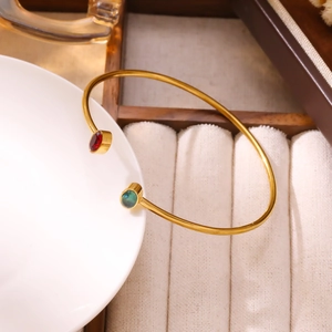 Dettaglio del bracciale rigido dorato con pietre ovali rosse e verdi in esposizione