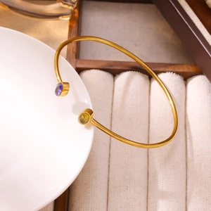 Dettaglio di un bracciale rigido dorato con pietre preziose rotonde viola e giallo-verde