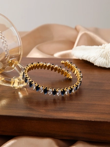 Dettaglio di un bracciale a spirale dorato con zirconi marquise blu e trasparenti