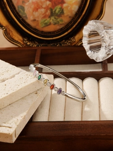 Detail view of silver stainless steel bangle featuring colorful oval cubic zirconia stones