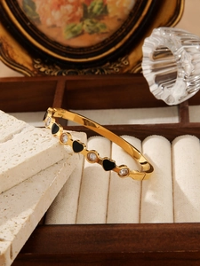 Detail showing gold bangle with black heart shapes and clear cubic zirconia stones