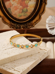 Detailed close-up of golden bangle featuring blue enamel hearts and round zircon stones