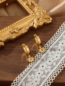 Detailed macro of golden sunflower earrings with purple zircon on vintage silk and lace