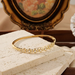 Golden stainless steel bangle with sparkling cubic zirconia on white stone textures