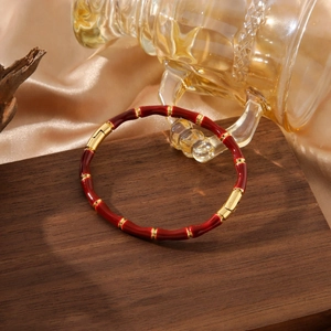 Gold bamboo-style bangle with red enamel inlay and two secure clasps on wood display