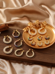 Primer plano de aretes de aro dorados de acero con cristales de colores y perlas finas