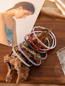 Stack of colorful rhinestone elastic bracelets displayed on natural wood with silk fabric