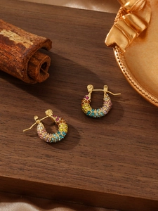 Detalle de pendientes de aro dorados en forma de C con cristales de colores en madera
