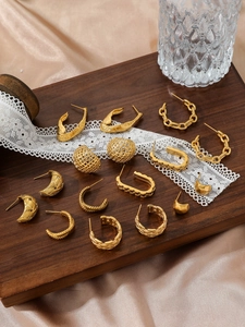 Detailed view of assorted gold chain link and woven texture earrings on a wooden tray