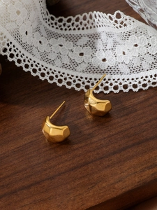 Close-up of golden stainless steel earrings with geometric rock texture on wood background