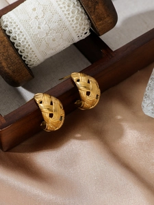 Detailed view of golden C-shaped hoop earrings with intricate woven texture on wood