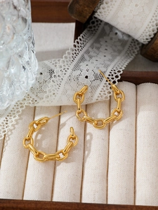Detailed close-up of golden chain-link C-shaped stainless steel earrings on velvet