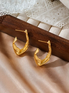 Close-up of golden C-shaped hoop earrings with lava texture on silk background