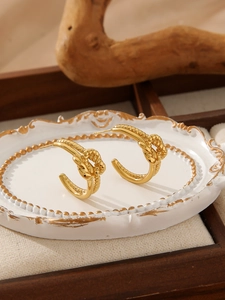 Detailed view of irregular gold-plated knot hoop earrings on an elegant vintage tray
