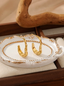 Close-up of golden irregular lava texture hoop earrings on a vintage relief tray