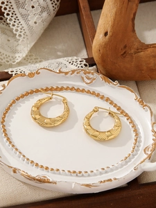 Close-up of golden wide hoop earrings with embossed texture on an elegant white tray